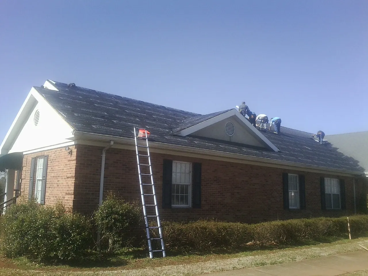 Crew tearing shingles off a brick ranch roof with a ladder set — Emergency Roof Repair work by our crew in Emerson