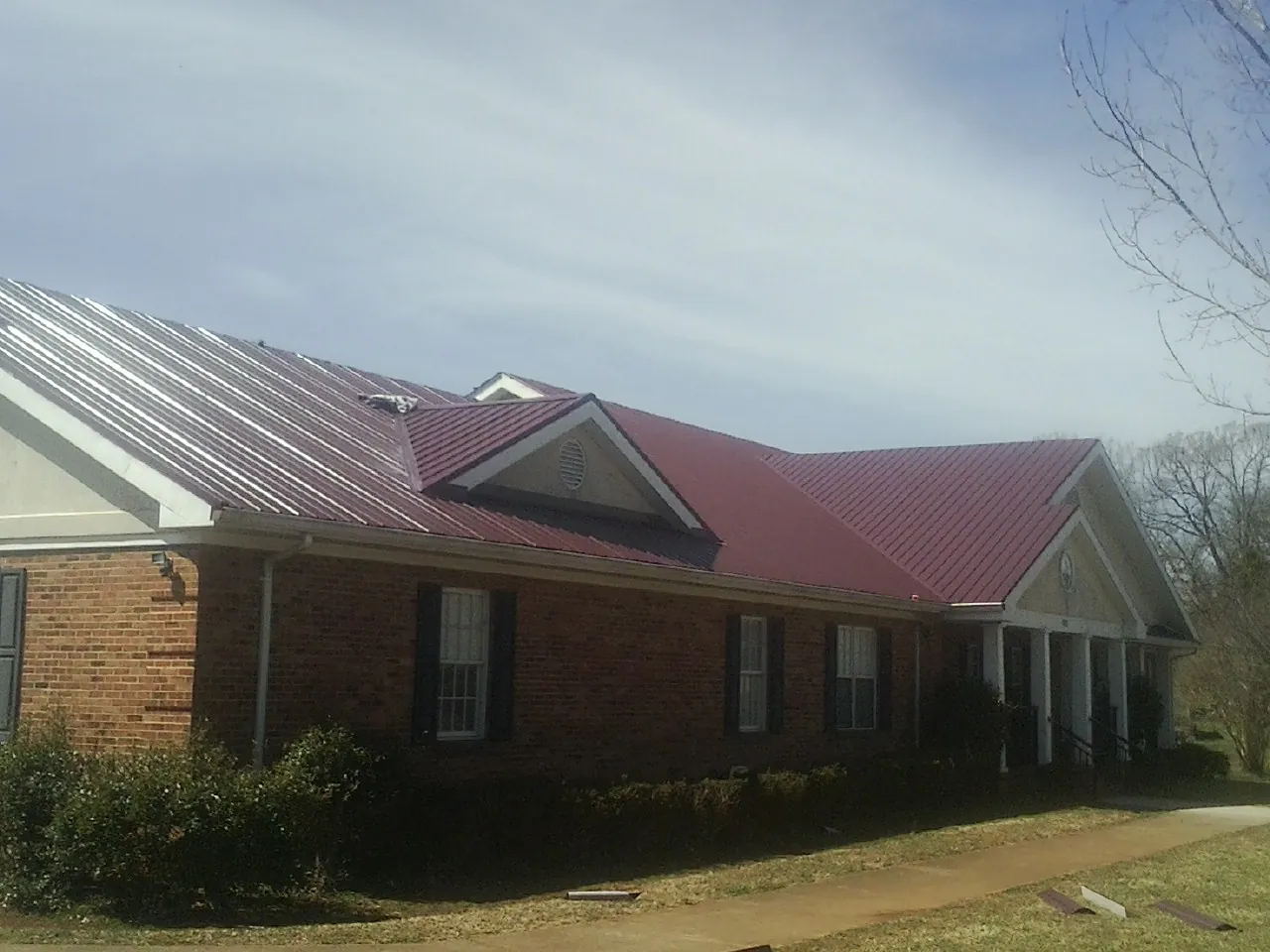 Red metal roof with gabled entries on a long brick building, from a Hail Damage Roof Repair job in Emerson