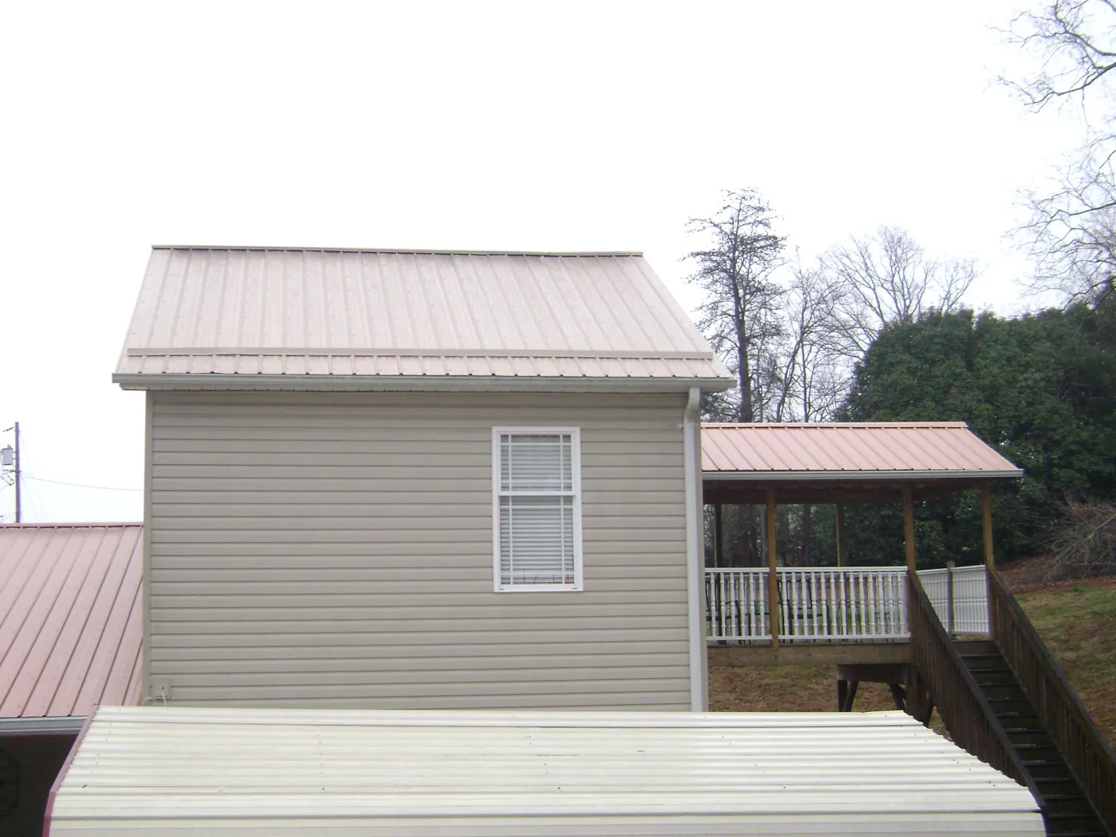 Tan metal roofs on a two story addition and attached porch, from a Roof Replacement job in Emerson